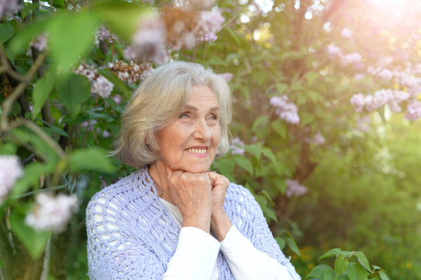  senior beautiful woman posing with lilacs in   park - Фото, изображение