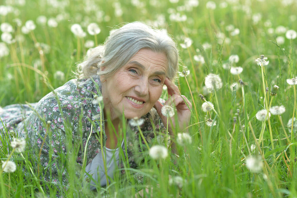 Portrait of a beautiful senior woman in green field with dandelions - Fotografie, Obrázek