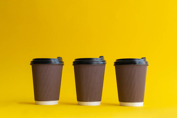 Three takeaway brown paper coffee cups with black plastic covers - Foto, afbeelding