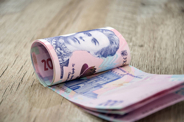 Neue Banknoten mit einem Nennwert von 200 Griwna auf einem hölzernen Hintergrund zusammengerollt. Ukrainisches Geld. Geschäftskonzept. Sparkonzept oder Sparkonzept - Foto, Bild