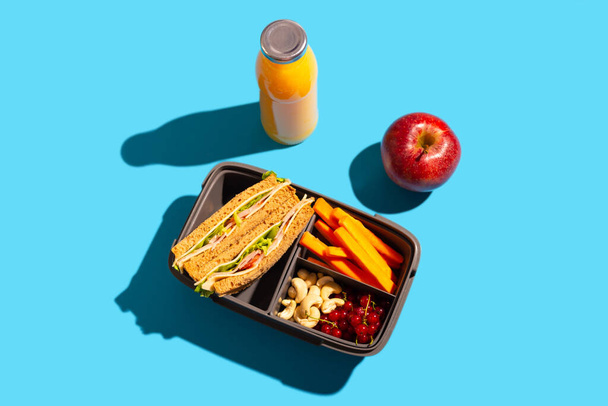 Almuerzo escolar saludable en un contenedor conveniente sobre un fondo azul brillante
. - Foto, imagen