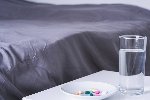 Tabaktaki hapları kapat ve yatak odasındaki komodinin üzerine bir bardak su koy. Sağlık ve tıbbi eczane kavramı - Fotoğraf, Görsel