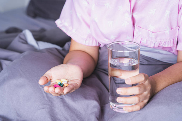 Sluit een vrouwelijke patiënt met een glas water en pillen in de slaapkamer. Gezondheidszorg en medisch apothekersconcept - Foto, afbeelding