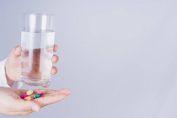Acercamiento mujer asiática sosteniendo un vaso de agua y pastillas en la mano sobre fondo gris. Concepto de atención sanitaria y farmacia médica
 - Foto, imagen