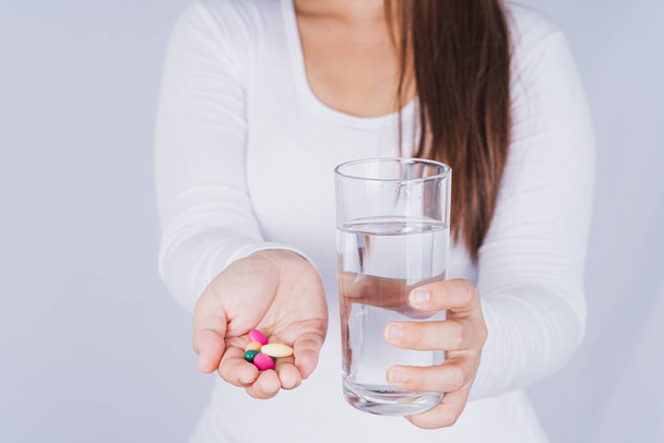 Закройте азиатку с стаканом воды и таблетками в руке на сером фоне. Здравоохранение и медицинская аптека
 - Фото, изображение