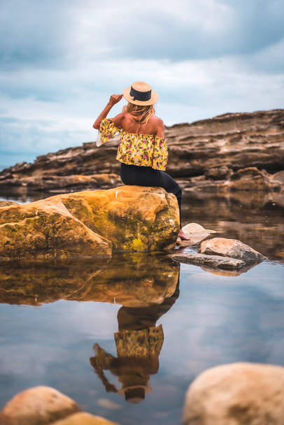 Happy relaxed woman in hat at rocky shore. Summer vacation concept - Zdjęcie, obraz