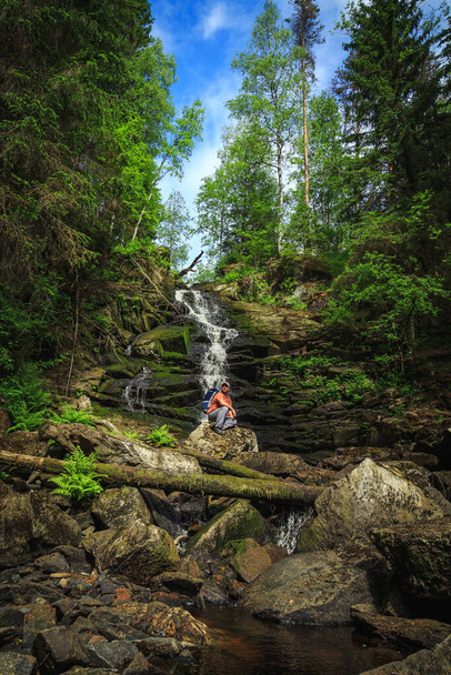 Tourist sits on a rock near a forest waterfall. Feeling of relaxation and freedom. - Foto, immagini