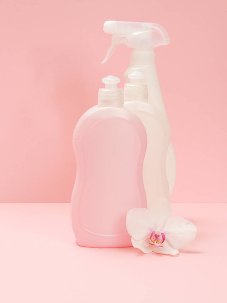 Plastic bottles of dishwashing liquid, glass and tile cleaner and a white orchid flower on a pink background. Washing and cleaning set. - Фото, зображення