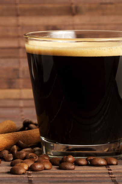 Espresso lyhyessä lasissa kahvipapuja ja kanelia puolelta
 - Valokuva, kuva