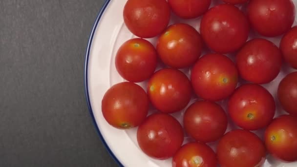 Beyaz tabakta vişneli domatesler. Gri taştan bir yüzeye yakın mavi bir kenarı var. Çiy tanesiyle olgunlaşmış kırmızı sebze. Yavaş döndürme - Video, Çekim