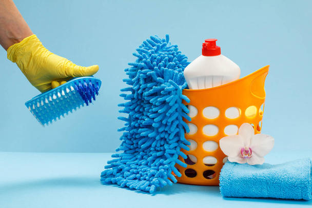 Mano de mujer en guante protector de nitrilo sosteniendo un cepillo con un conjunto de lavado y limpieza sobre el fondo azul
. - Foto, imagen