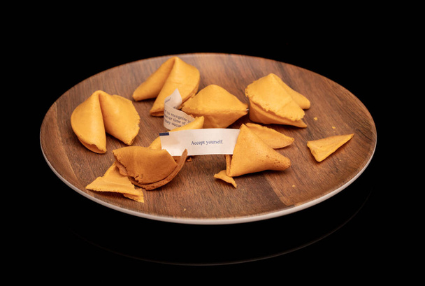 Crisp and sugary fortune cookies on wooden brown plate isolated on black - Фото, изображение