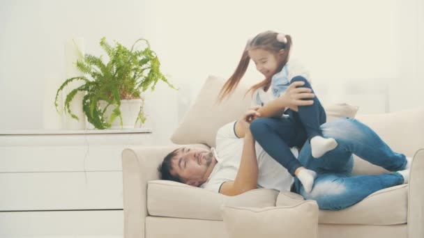 4k slowmotion video where father really wants to have a good sleep but his little daughter sitting on his legs. - Materiał filmowy, wideo