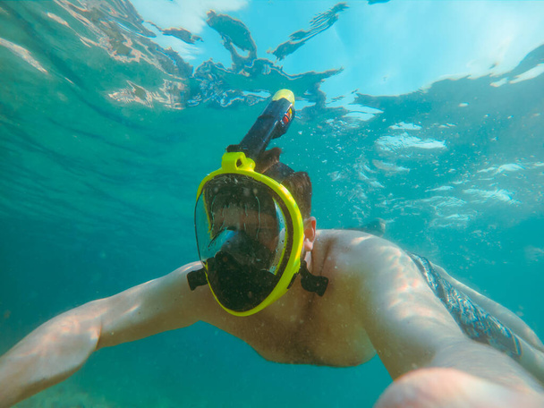 Şnorkel maskeli bir adam yaz tatili için açık şeffaf su kullanıyor. - Fotoğraf, Görsel