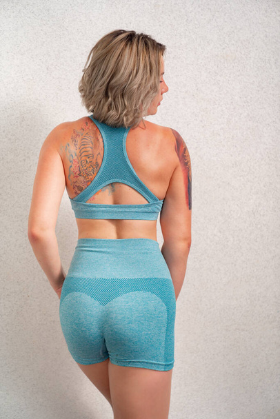 girl with tattoo in sportswear is engaged in home fitness, posing against wall. - Foto, immagini