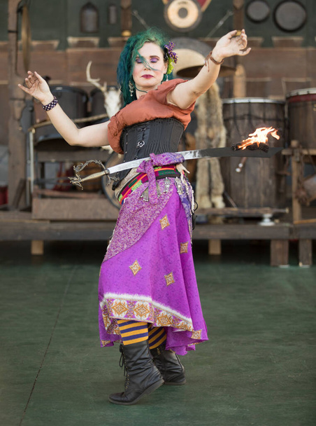 Красивая зеленая женщина в костюме танцует на сцене с горящим мечом - Фото, изображение