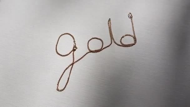 Gouden tekst van een gouden ketting op een witte zonnige tafel. Bovenaanzicht - Video