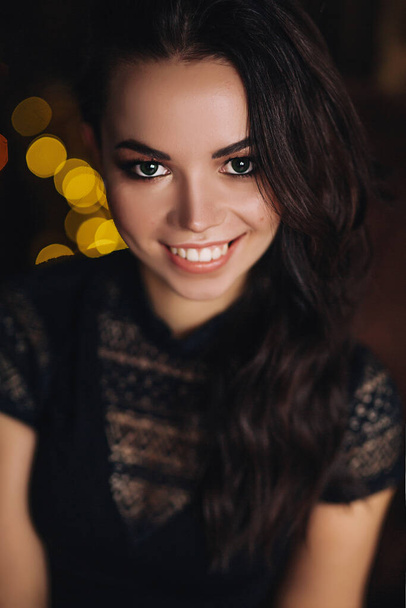 Portrait of young european woman in dark studio with lights, pretty caucasian lady in black wear with long dark hair and bright makeup, she is smiling - Φωτογραφία, εικόνα