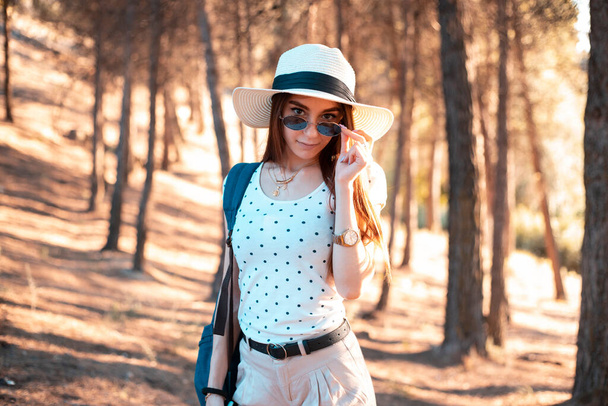 молода дівчина з капелюхом і рюкзаком подорожує в лісі
 - Фото, зображення