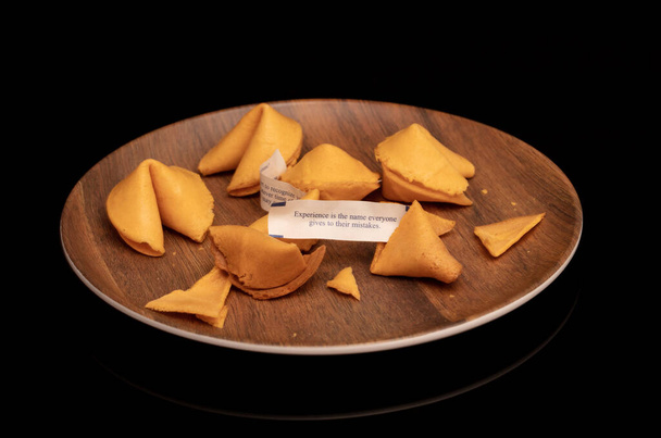 Crisp and sugary fortune cookies on wooden brown plate isolated on black - Photo, Image