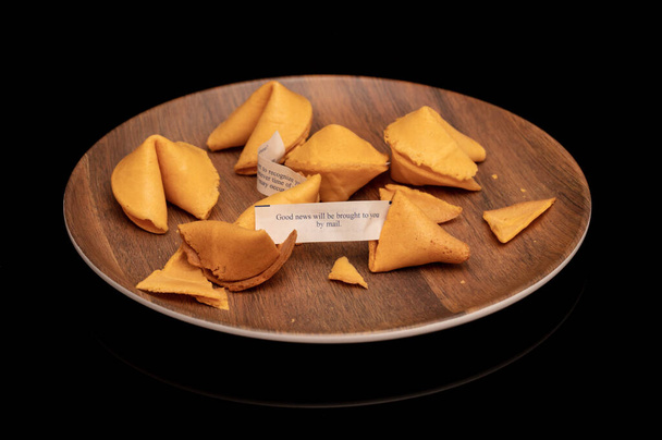 Biscotti della fortuna croccanti e zuccherati su piastra marrone in legno isolata su nero - Foto, immagini