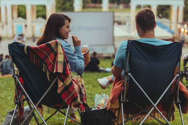 couple assis dans des chaises de camp dans le parc de la ville à la recherche de film en plein air au cinéma en plein air style de vie - Photo, image