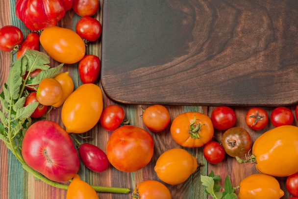 Sorte frische bunte Tomaten. Ökologischer Landbau ist umweltfreundlich. Gruppe frischer Tomaten und Schneidebrett aus Holz - Foto, Bild