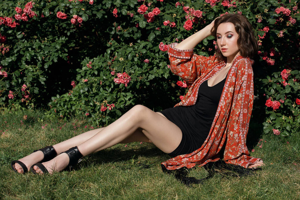 Mladá hezká modelka pózuje v růžové zahradě. Venkovní portrét romantické dívky s tvrdým slunečním světlem. - Fotografie, Obrázek