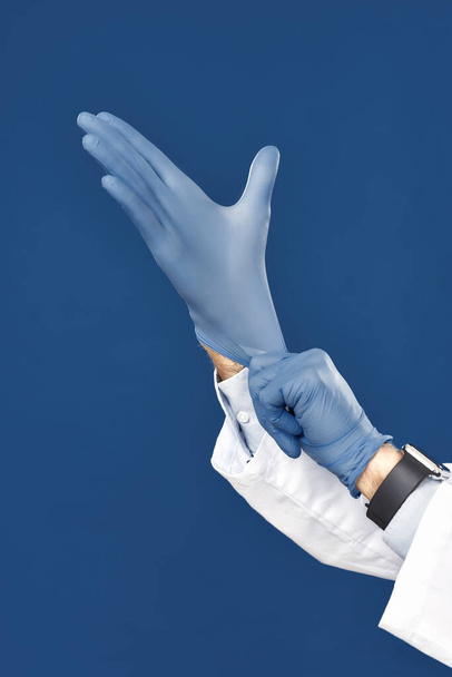 Protection. Cropped shot of male doctor hands putting on blue sterile gloves, isolated against navy blue background - Foto, imagen