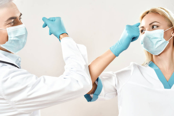 Instead of handshaking. Male and female doctors wearing protective face masks greeting each other by bumping elbows, standing against grey background - Foto, Bild