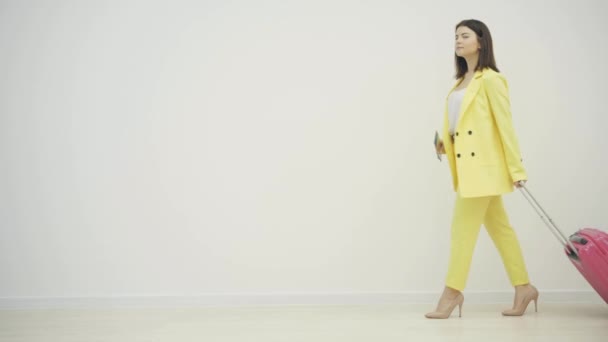 Young successful businesswoman looking stylish, wearing classical suit and carrying a big suitcase over white background. - Materiał filmowy, wideo
