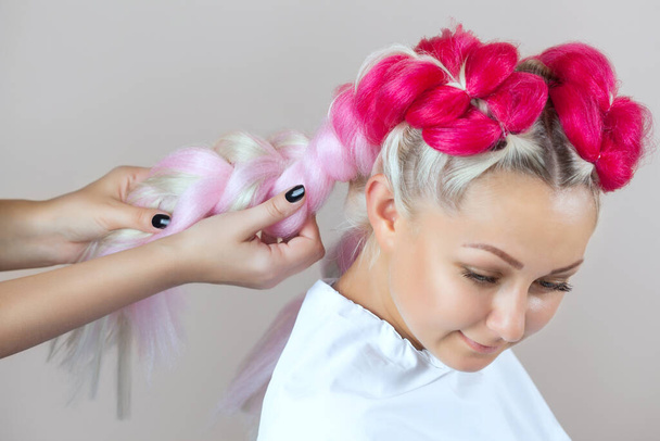 Парикмахерская плетет косички с розовыми канекалонами красивая блондинка салон красоты. - Фото, изображение