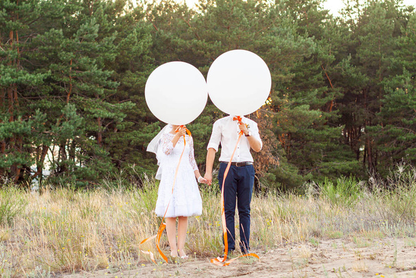 Bride and groom holding big white helium baloons with orange ribbons in the forest. Wedding idea concept, background - Foto, imagen