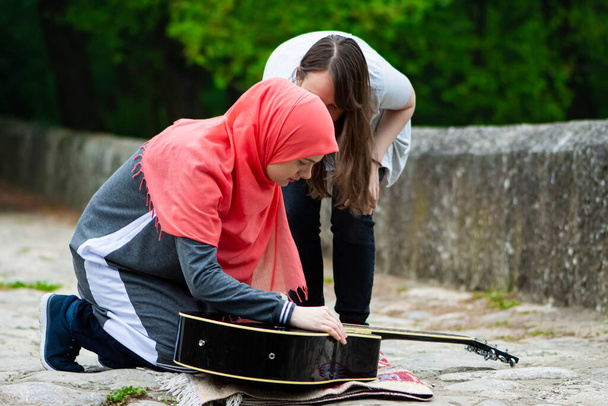 2人のイスラム教徒の女の子何かを探しているギターの屋外 - 写真・画像