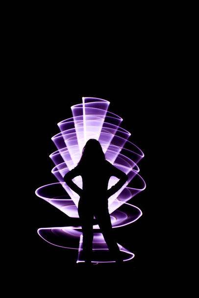 Silueta ženy s vedeným světlem. Zakřivený abstraktní tvar vyrobený ze světlé fialové šavle. Lightpainting session v noci - Fotografie, Obrázek