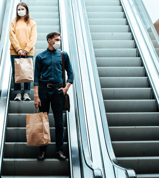 young man in a protective mask standing on an escalator in a shopping center - Photo, image
