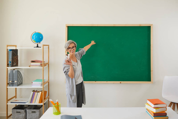 School education. Senior teacher explaining material near blackboard at clasroom. Mature professor giving lecture online - Фото, зображення