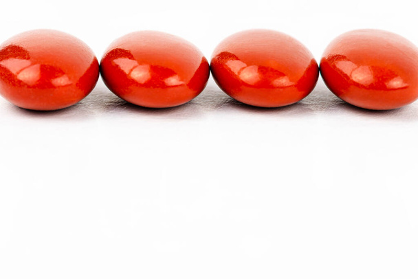 Plan macro de quatre comprimés pelliculés rouges disposés en rangée sur le dessus, isolés sur un fond blanc. - Photo, image