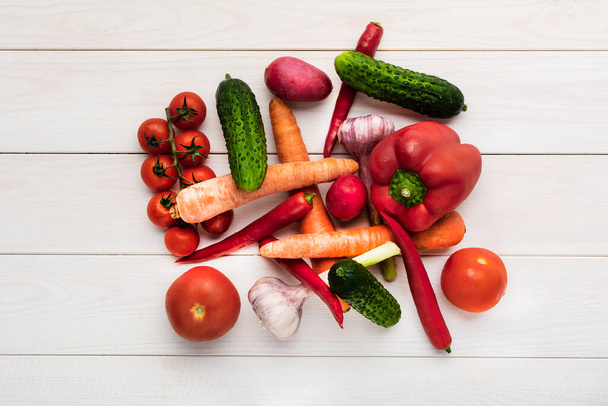 Various raw vegetables on a white wooden background with blank space around. Zucchini, cucumber, chili pepper, mushrooms, tomatoes, cauliflower, lettuce, carrots, celery, garlic, radishes paprika - Fotografie, Obrázek