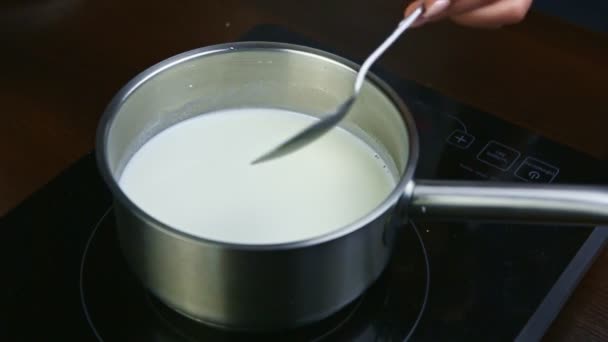 スローモーション閉じ女性の手によってスプーンは金属鍋で沸騰ミルクを攪拌 - 映像、動画
