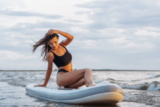 Giovane surfista donna sexy seduto sulla sua tavola da sup. Riposare sul concetto di natura - Foto, immagini