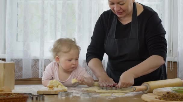 Mamie biscuits de coupe de pâte crue de pain d'épice et la petite-fille goûte la pâte. - Séquence, vidéo