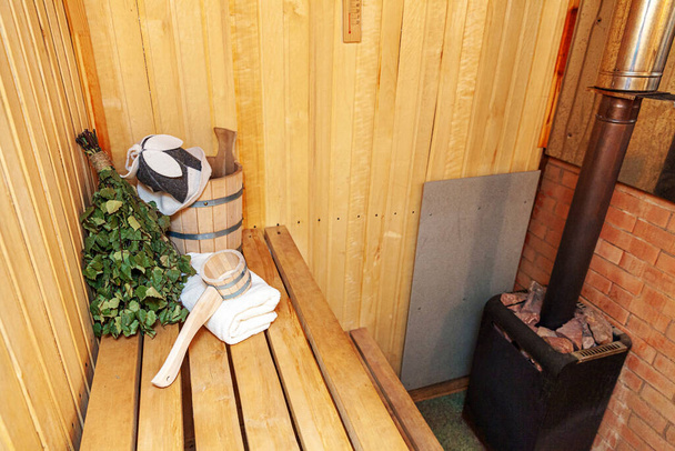 Detail interiéru Finská sauna parní lázeň s tradičním saunovým příslušenstvím povodí březové koště naběračka plstěný klobouk ručník. Tradiční stará ruská lázeňská koncepce lázní. Relax country vesnice lázně koncept. - Fotografie, Obrázek
