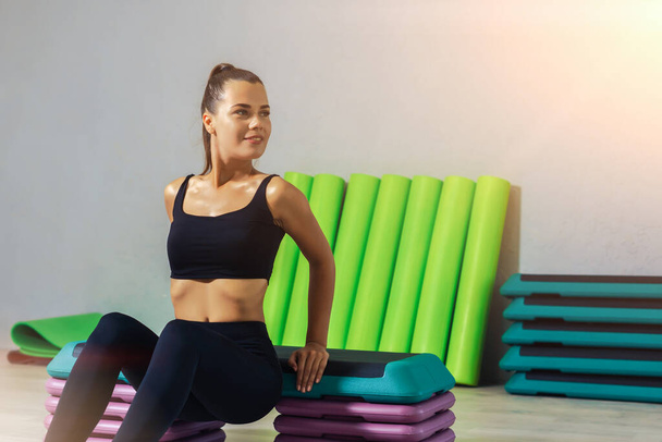 Jeune femme caucasienne faisant des pompes sur une plate-forme étape dans un studio de fitness. Concept de mode de vie sain.  - Photo, image