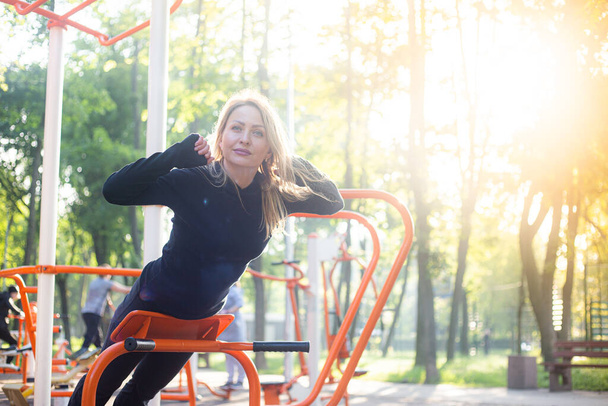 Девушка на летней спортивной площадке занимается спортивными упражнениями для спины
 - Фото, изображение