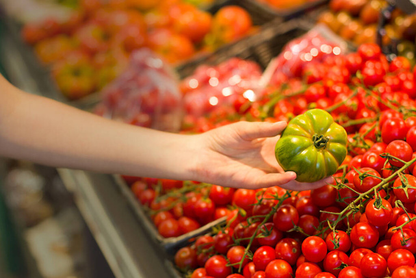 Mano femenina eligiendo tomate en el supermercado. Concepto de alimentación saludable, bio, vegetariano, dieta
. - Foto, Imagen