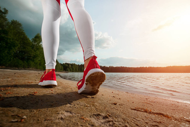 Beine eines Mädchens in Trainingsanzug Nahaufnahme, läuft entlang des Weges eines Sees oder Meeres. Das Konzept eines gesunden Lebensstils, Cardio Workout. Kopierraum - Foto, Bild