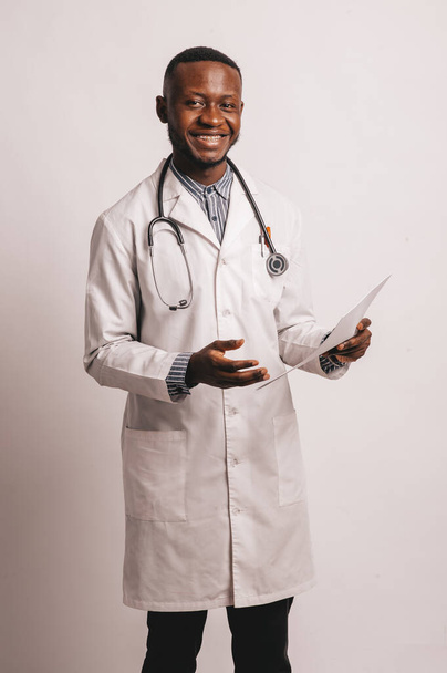 black skinned young medic smiling standing on a white background with papers in hand - Фото, изображение