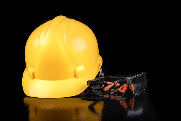 Yellow work helmet and safety glasses. Workwear for the production worker. Dark background. - Fotó, kép