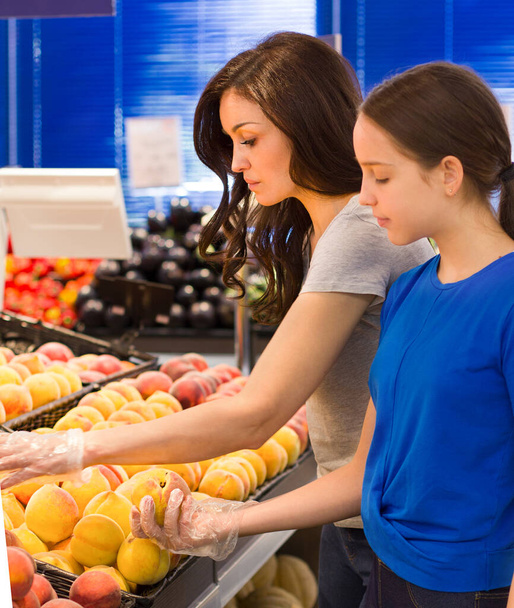 Mother and daughter shopping in supermarket, reading product information. Choosing daily product - Photo, Image